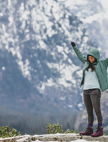 a woman standing on top of a snow covered mountain with her arms up in excitement