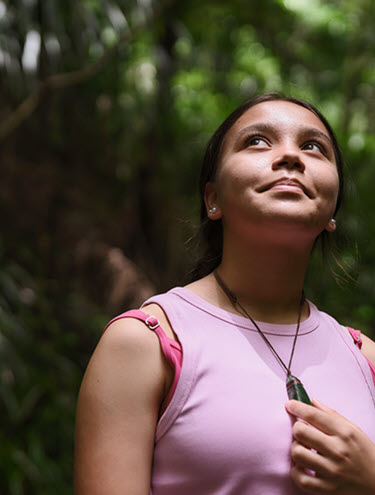 Young woman in a pink top stands amidst lush green foliage in a New Zealand forest, embodying the spirit of nature and sustainability