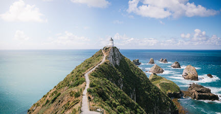 The iconic Nugget Point lighthouse perched on a narrow promontory with rocky formations in the ocean below in the Catlins.