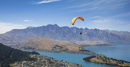 A paraglider soaring over Queenstown with a view of the lake and surrounding mountains.