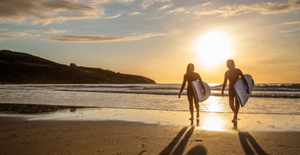 Two surfers walking along the beach at sunset