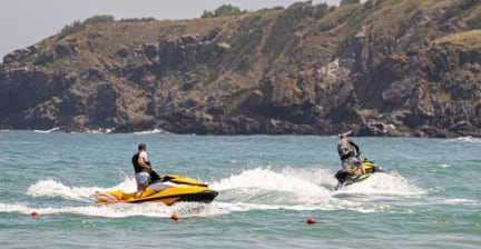 Two people riding jet skis in the ocean near a rocky coastline