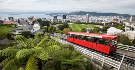 Red cable car going uphill with a view of the city and ocean in the background