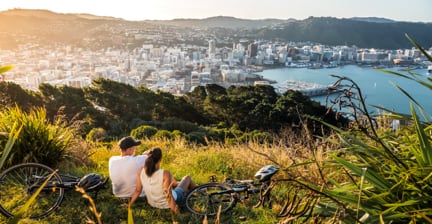 Couple relaxing with bicycles, overlooking Wellington city from a hill at sunset