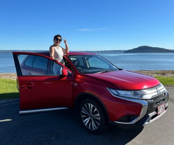 Woman standing next to an open GO Rentals red car door, parked near a lake with a mountain in the distance