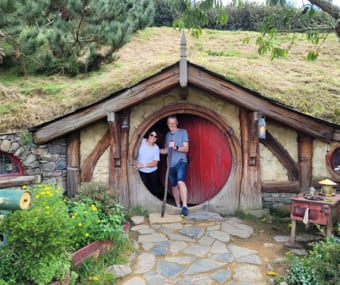 Two people posing in front of a Hobbit house from The Lord of the Rings movie set