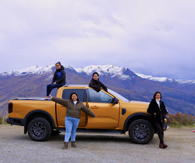 Four people with a yellow truck on a mountain road