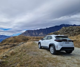 White GO Rentals SUV parked on a mountain trail with a backdrop of cloudy skies and hills