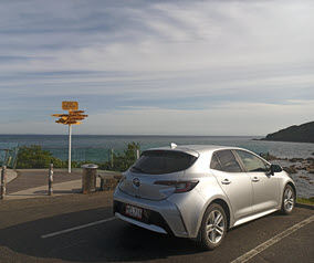 Silver car by the ocean with a signpost