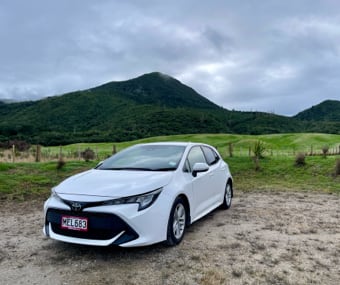 White GO Rentals car parked on a dirt road with a green hill in the background