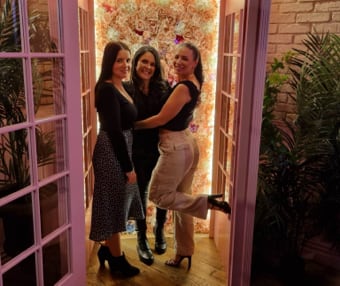 Three women posing together in front of a floral backdrop at an event