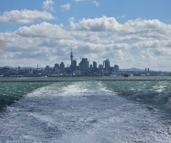 View of a city skyline from the water, with a trail of waves behind a boat